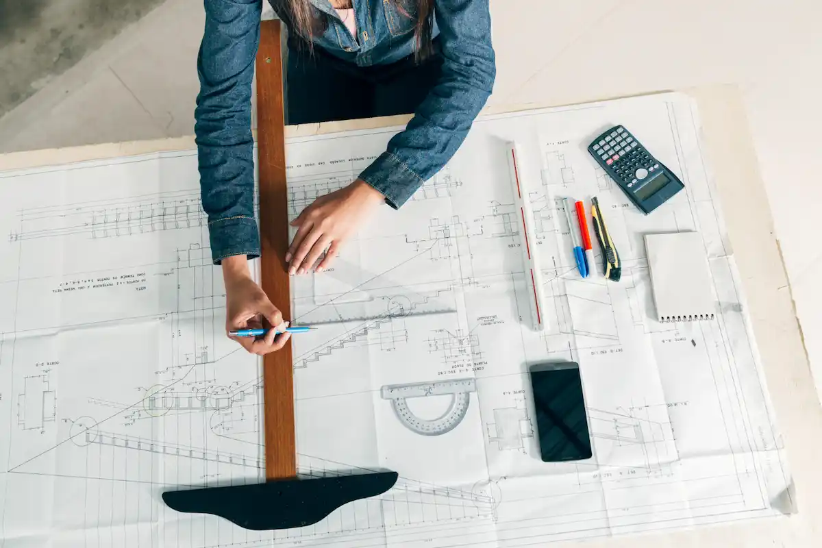 Structural draftsman using architectural tools to design building layout blueprints on a work desk.